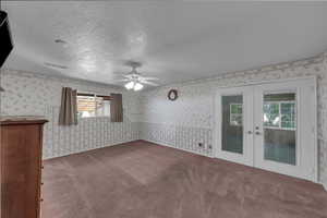 Carpeted spare room featuring french doors, a textured ceiling, ceiling fan, and wallpapered walls