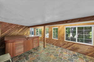 Additional living space featuring stone flooring, a textured ceiling, and wood walls