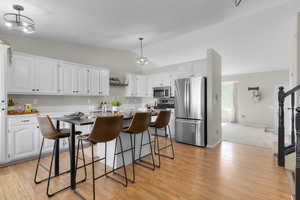Kitchen featuring appliances with stainless steel finishes, lofted ceiling, white cabinets, and light wood finished floors