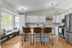 Kitchen with stainless steel appliances, lofted ceiling, white cabinetry, a breakfast bar area, and light wood-style flooring