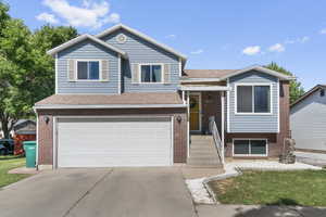 Split level home featuring an attached garage, driveway, brick siding, and a shingled roof