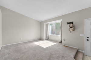 Empty room featuring light colored carpet and vaulted ceiling