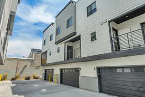 Back of house featuring an attached garage, a balcony, and driveway