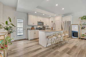 Kitchen with stainless steel appliances, a kitchen bar, light wood-style flooring, a center island with sink, and recessed lighting