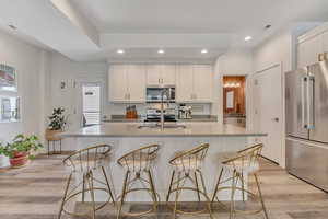 Kitchen with stainless steel appliances, recessed lighting, light wood-type flooring, a kitchen bar, and an island with sink