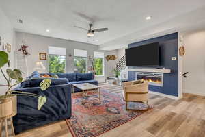 Living area featuring stairway, a textured ceiling, wood finished floors, a ceiling fan, and a glass covered fireplace