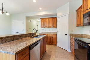 Kitchen with black appliances, brown cabinets, light stone counters, light tile patterned floors, and recessed lighting