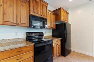 Kitchen featuring black appliances, brown cabinets, light stone counters, and light tile patterned flooring
