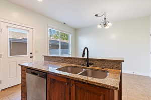 Kitchen featuring stainless steel dishwasher, light tile patterned floors, hanging light fixtures, and light stone countertops