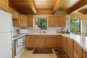 Kitchen featuring light flooring, white appliances, a wood ceiling with exposed beams, light countertops, and a peninsula