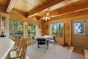 Dining space featuring a wood ceiling with exposed beams, a ceiling fan, wood walls, and light colored carpet