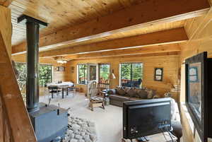 Living area featuring a wood stove, wooden walls, a wood ceiling with exposed beams, carpet floors, and a ceiling fan