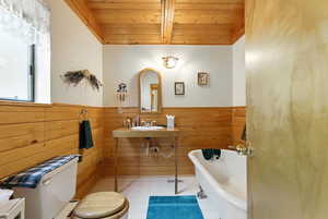 Full bathroom featuring a freestanding tub, tile patterned floors, wooden ceiling, wooden walls, and a wainscoted wall