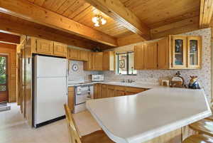 Kitchen featuring light floors, a peninsula, white appliances, glass insert cabinets, and light countertops