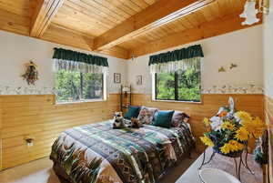 Bedroom featuring wainscoting, multiple windows, a wooden ceiling with exposed beams, carpet floors, and wood walls