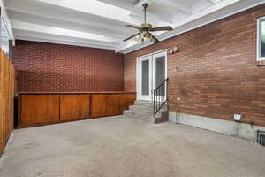 Empty room with brick wall, beam ceiling, carpet flooring, and ceiling fan