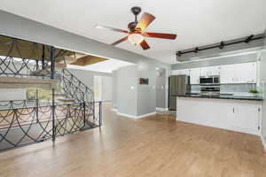 Unfurnished living room with stairs, light wood-style floors, and a ceiling fan