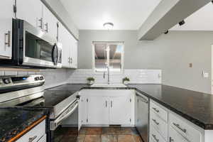 Kitchen with appliances with stainless steel finishes, a peninsula, dark countertops, and backsplash