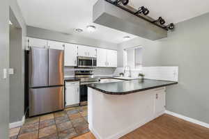 Kitchen with appliances with stainless steel finishes, a peninsula, tasteful backsplash, and white cabinets