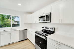 Kitchen featuring appliances with stainless steel finishes, white cabinetry, light wood-style flooring, and recessed lighting