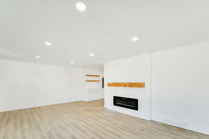 Unfurnished living room with light wood-style flooring, a large fireplace, and recessed lighting