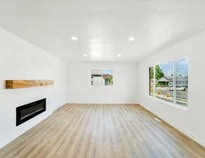 Unfurnished living room with light wood-type flooring, a large fireplace, and recessed lighting