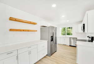 Kitchen with open shelves, white cabinets, appliances with stainless steel finishes, recessed lighting, and light wood-style floors
