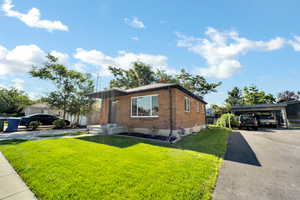 View of front facade featuring brick siding, a front lawn, driveway, and a chimney