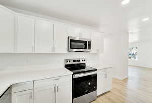 Kitchen with stainless steel appliances, white cabinets, light wood-style floors, and recessed lighting