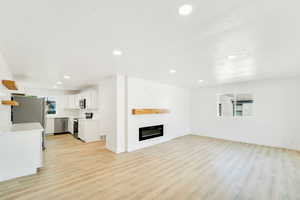 Unfurnished living room featuring plenty of natural light, light wood-style floors, recessed lighting, and a large fireplace