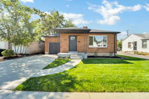View of front facade with brick siding, driveway, a garage, a front lawn, and a chimney
