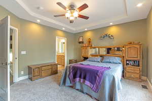 Bedroom featuring recessed lighting, light colored carpet, a raised ceiling, and connected bathroom