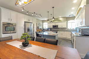 Kitchen with stainless steel appliances, a kitchen island, white cabinets, tasteful backsplash, and decorative light fixtures