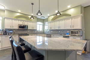 Kitchen with white cabinetry, appliances with stainless steel finishes, a center island, decorative backsplash, and a kitchen bar