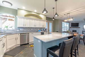 Kitchen with stainless steel dishwasher, white cabinets, a stone fireplace, light stone countertops, and a kitchen island, french doors to back patio
