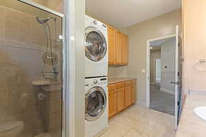 Full bath featuring stacked washer / drying machine, a stall shower, vanity, and tile patterned floors