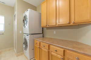 Bathroom with stacked washing machine and dryer, cabinet space, and light tile patterned floors