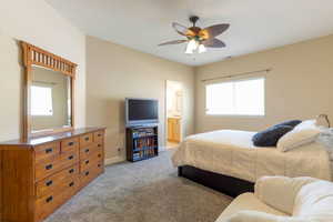 Bedroom with carpet flooring, a ceiling fan, and connected bathroom