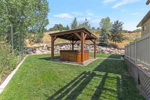 View of grassy yard with a hot tub and a gazebo