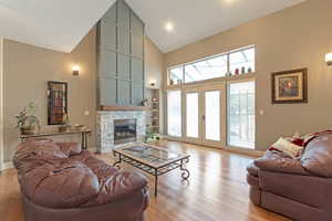 Living room featuring a fireplace, light wood-style flooring, high vaulted ceiling, built in features, and french doors