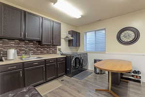 Laundry/Mudroom featuring cabinet space, washing machine and clothes dryer, light wood-style flooring, and a wainscoted wall