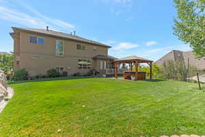 Back of house featuring a hot tub, a lawn, and stucco siding