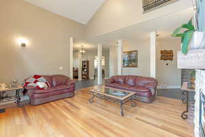Living area featuring high vaulted ceiling, a fireplace, a chandelier, and wood finished floors