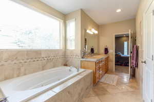 Ensuite bathroom featuring vanity, a tub with jets, tile patterned flooring, tile walls, and recessed lighting