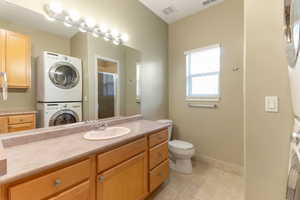 Full bath featuring stacked washer / drying machine, a stall shower, vanity, and tile patterned floors