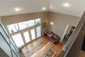 Living area featuring light wood-style floors, high vaulted ceiling, a textured ceiling, and french doors