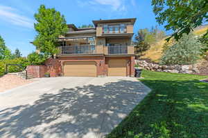View of front facade with a balcony, brick siding, stucco siding, driveway, and a front yard