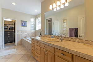 Full bath featuring a spacious closet, a bath, vanity, tile walls, and recessed lighting