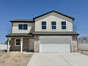 View of front facade with a garage, driveway, brick siding, board and batten siding, and a shingled roof