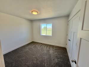 Unfurnished bedroom with dark colored carpet and a textured ceiling